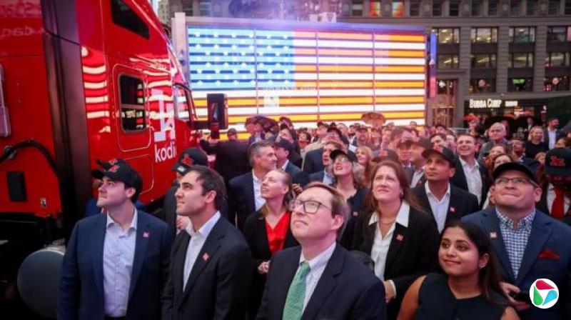 几位身穿西装的人站在时报广场,站在一辆印有“Kodiak AI”字样的红色卡车旁,抬头望向镜头外的上方。