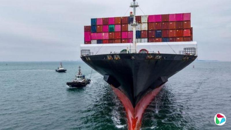 一艘大型货轮正驶离镜头,船上堆满了色彩鲜豔的货柜,包括亮粉红、红色、绿色和蓝色。