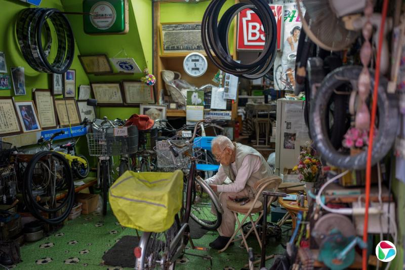 石井在东京的店铺里,正在修理顾客自行车上的车灯。