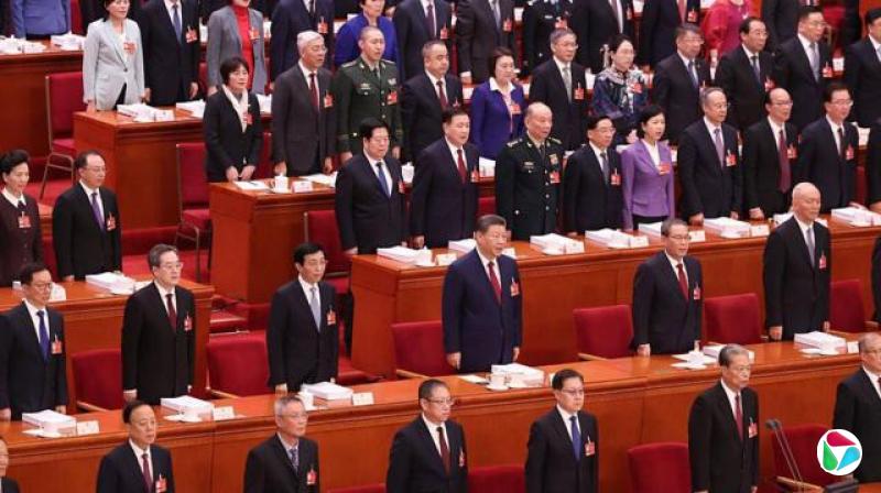 中国官员,包括位于图像中央的主席,在北京人民大会堂举行的全国人民代表大会开幕会上站在自己的座位旁