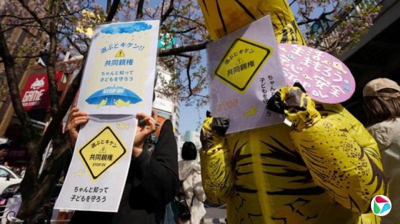 日本反家暴团体成员在东京新宿战士反对《民法》修正案“共同亲权”条款标语牌,其中一人(右)身穿恐龙装束(29/3/2026)