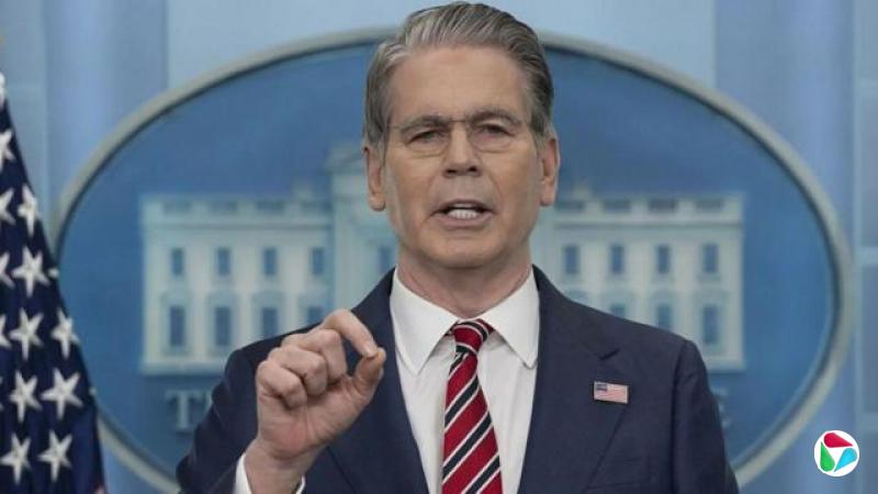 美国财政部长斯科特?贝森特(Scott Bessent)身穿蓝色西装、白色衬衫,配戴红、白及深蓝色条纹领带与美国国旗襟针,在白宫新闻简报室向镜头外的记者发表谈话。其身后可见美国国旗,并有一幅大型白宫影像,但多数被他的脸部与身体遮挡,下方印有“白宫”(The White House)字样。(15/4/2026)