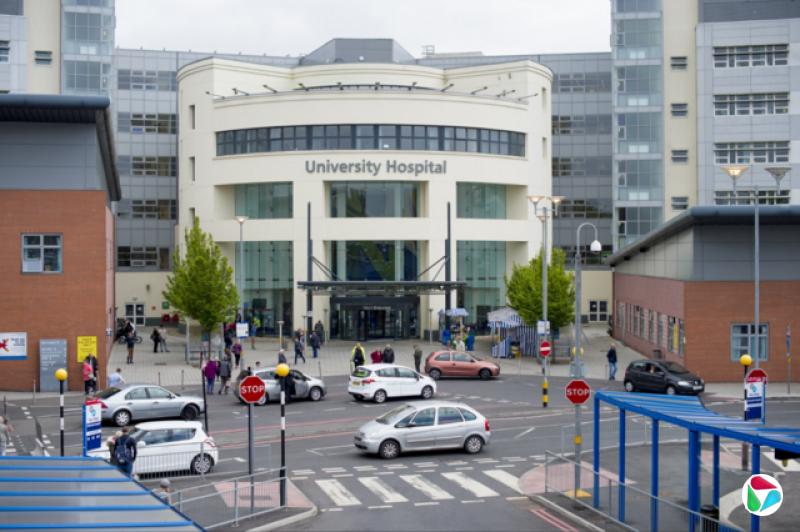 考文垂大学医院(University Hospital)外观。医院设有半圆形入口,配有窗户及宽阔大门,两侧为红砖建筑。门外停泊着多辆汽车。