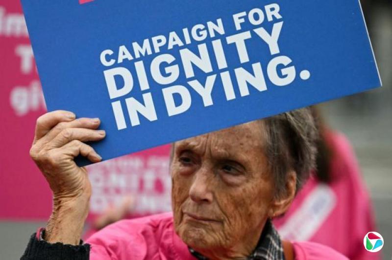 “尊严死亡”(Dignity in Dying)组织的一名倡议人士在英国国会所在地西敏宫外举行的示威活动中手持标语牌(16/10/2024)