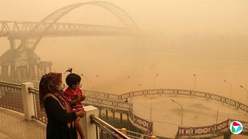 印尼中加里曼丹省帕朗卡拉亚地区,戴着口罩的母亲和孩子站在桥上眺望,森林和土地火灾产生的浓厚烟雾笼罩四周一切(12/10/2026)
