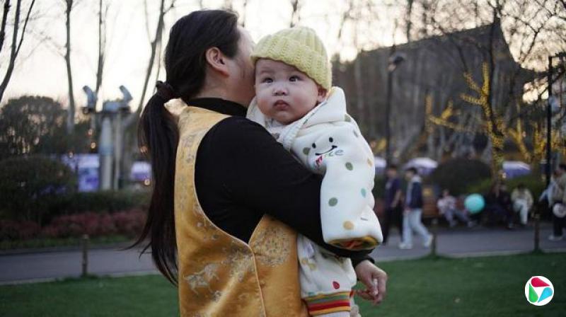 江苏常州,黄昏时分,公园里,一位穿着金色背心的女子抱着一个裹着波点毯子的婴儿(14/3/2026)